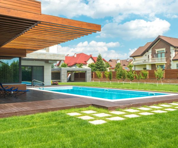 Stunning modern home exterior with a pool and well-maintained backyard under a blue sky.